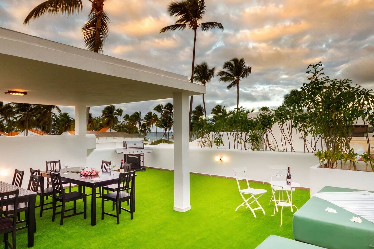 Une terrasse extérieure avec une table à manger pour six personnes, entourée de chaises, et un petit coin salon avec une table et des chaises.