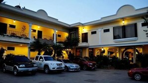Un hotel con un cortile interno, diverse auto parcheggiate e un ingresso ben illuminato.