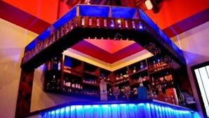 Un bar con un bancone curvo, scaffali pieni di bottiglie e un soffitto illuminato di blu.