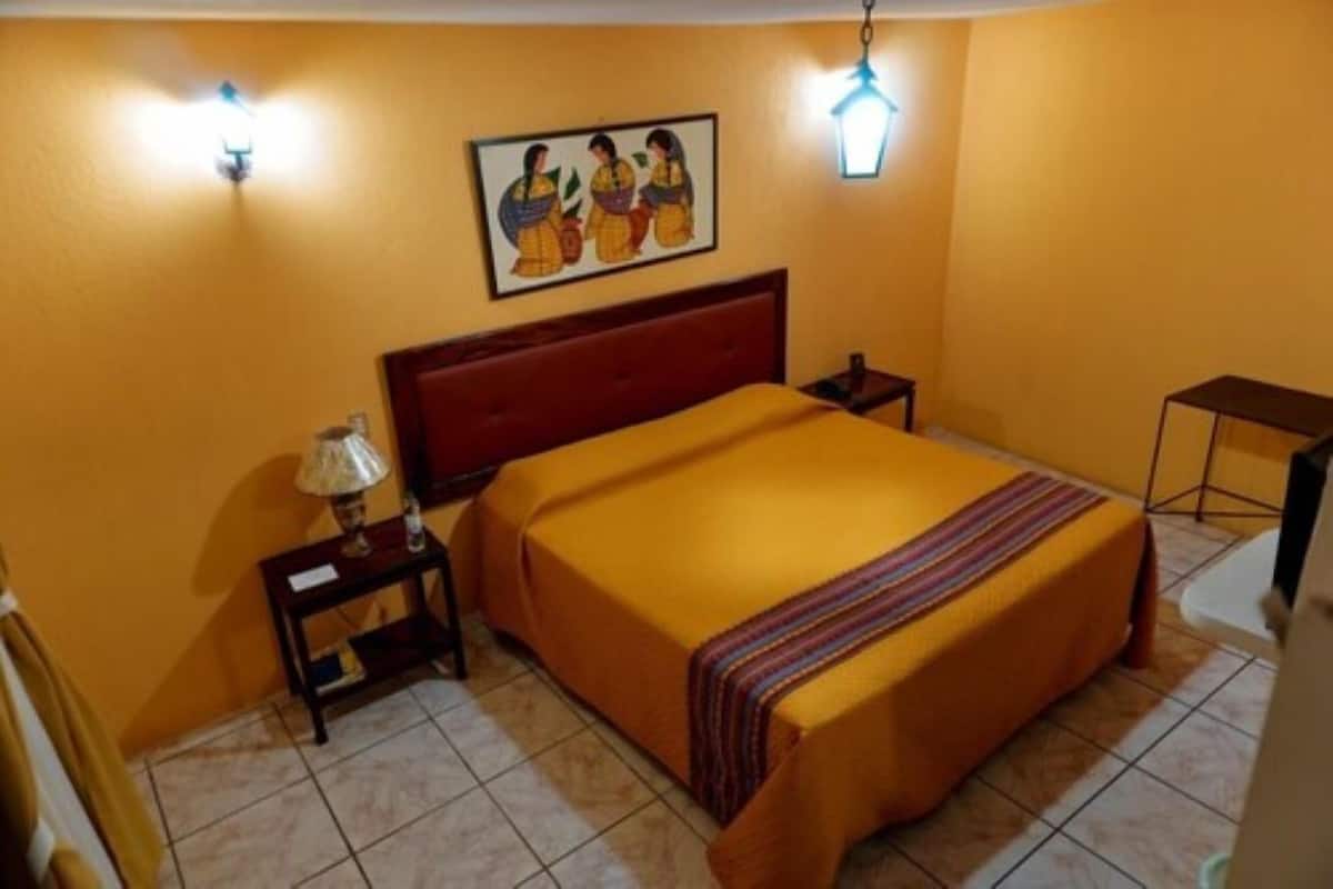 A room with a bed, a nightstand, a lamp, a painting on the wall, and a hanging light fixture.