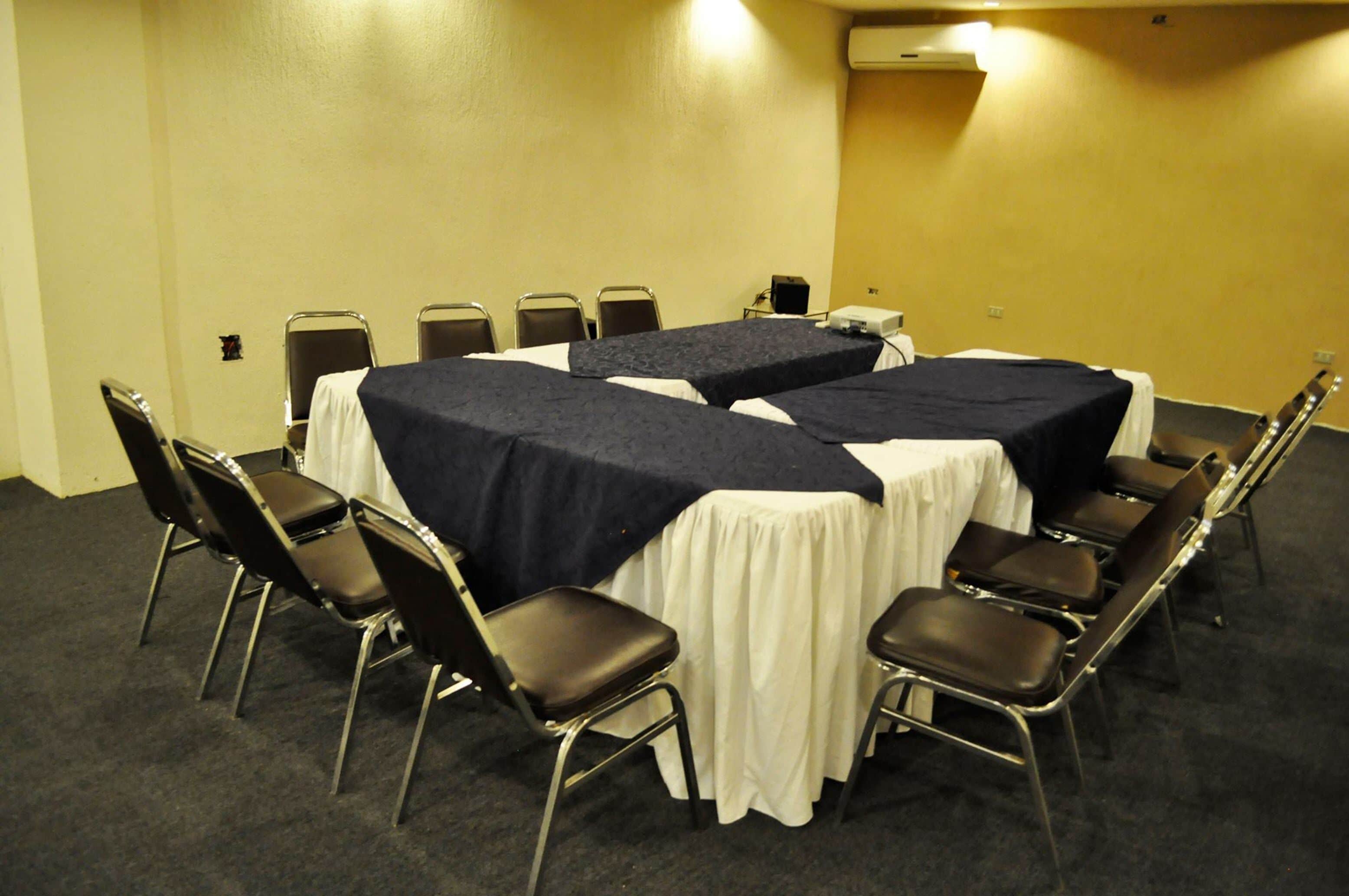 Una sala de conferencias con dos mesas cubiertas con manteles oscuros y blancos, rodeada de sillas negras.