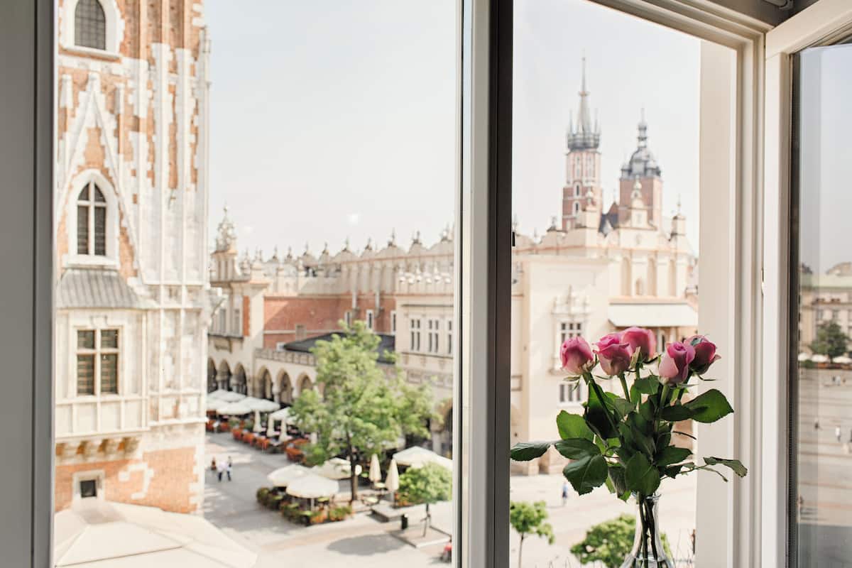 Vista desde una ventana de un edificio histórico con un florero de rosas en el alféizar.