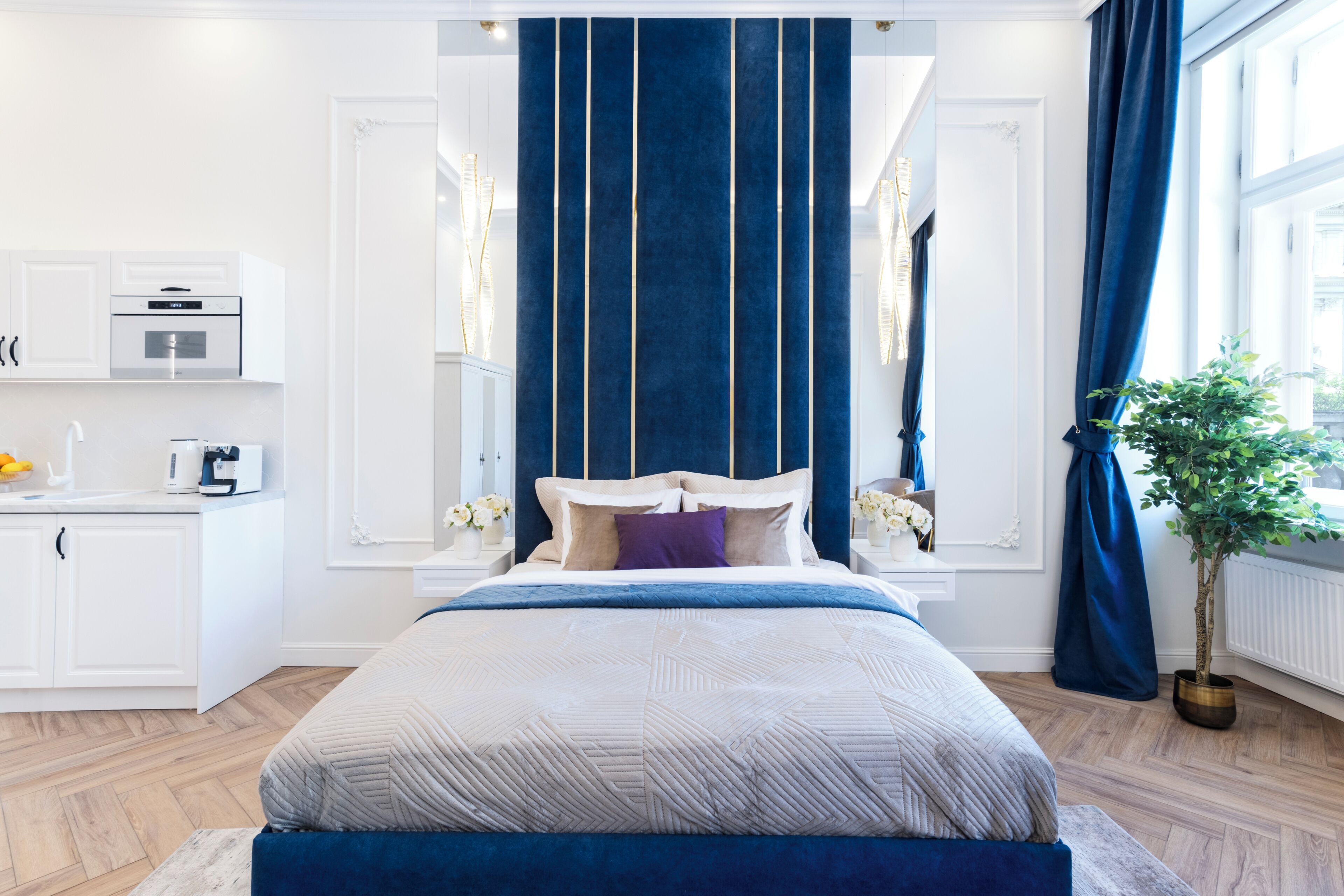 A bedroom with a bed, a nightstand, a dresser, a window with curtains, and a potted plant.