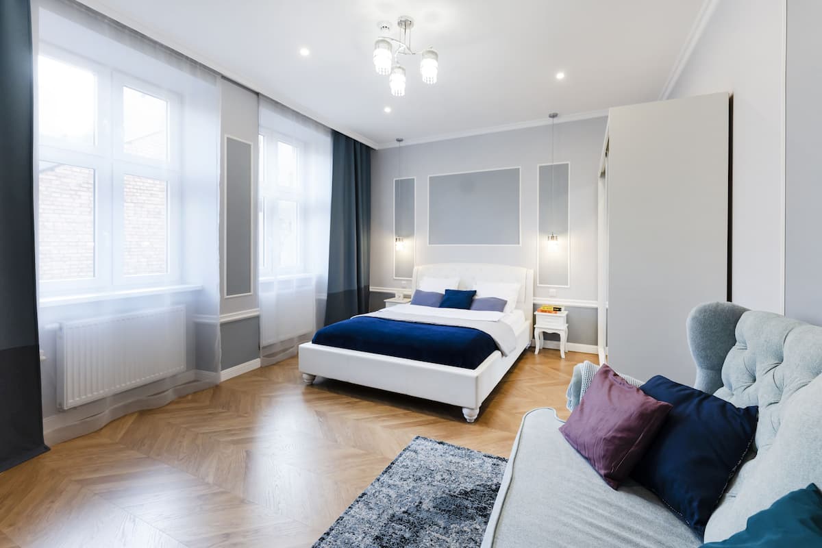 Un dormitorio moderno con una cama grande, un sofá gris y una ventana con cortinas.