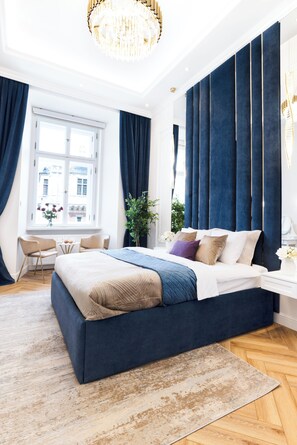 Un dormitorio moderno con una cama grande, una araña, una ventana con cortinas y una pequeña mesa con sillas.