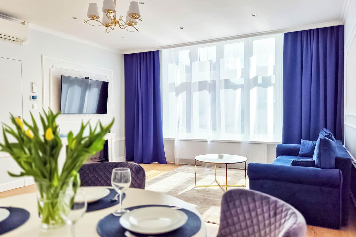 Una sala de estar moderna con un sofá azul, una mesa de comedor con platos y vasos, y un televisor instalado en la pared.