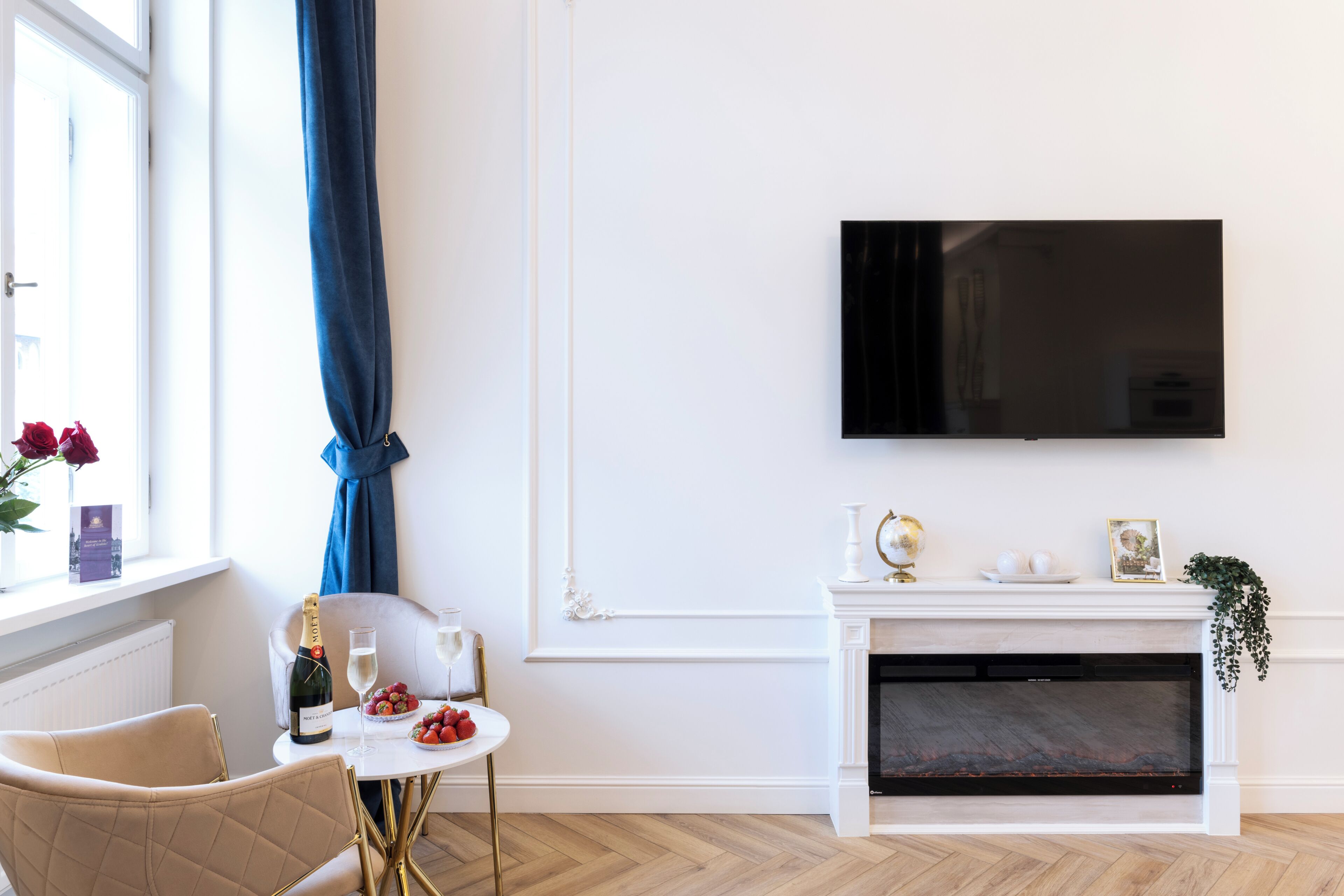 A modern living room with a fireplace, a television mounted on the wall, and a dining area with a table set for two.