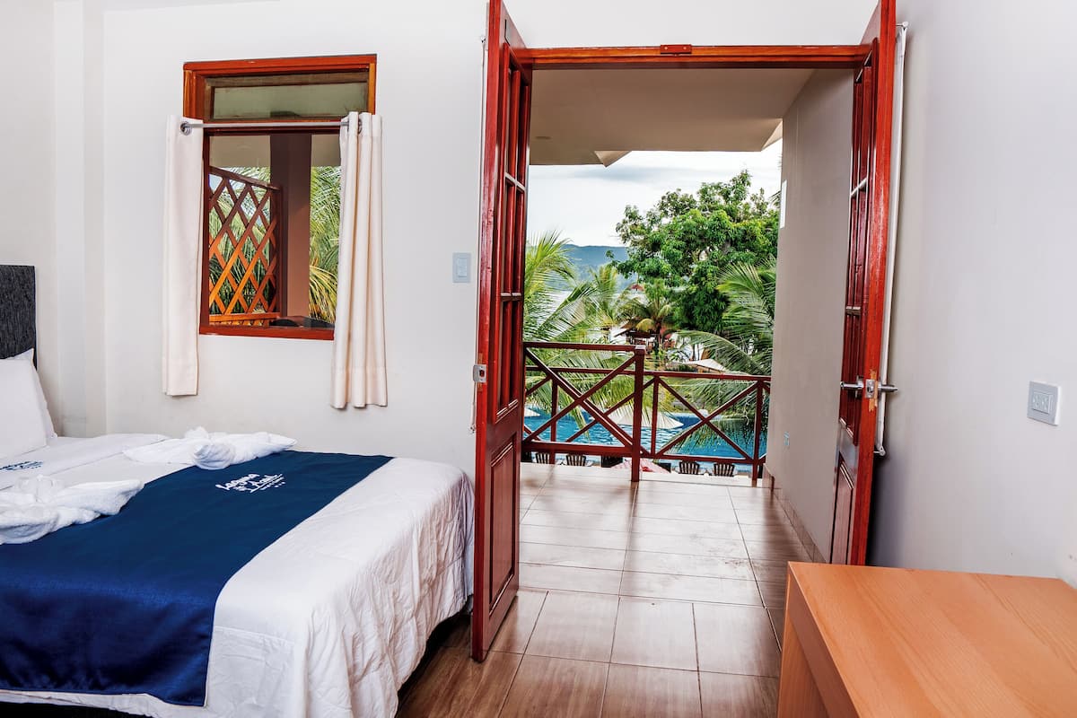 Habitación de hotel con cama, escritorio de madera y vista a una piscina y palmeras.