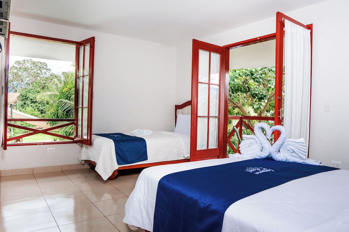 Habitación de hotel con dos camas, balcón y vistas a zonas verdes.