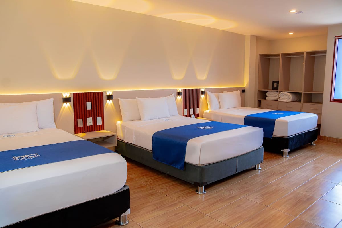 Una habitación de hotel con tres camas, un armario y un ventanal grande.