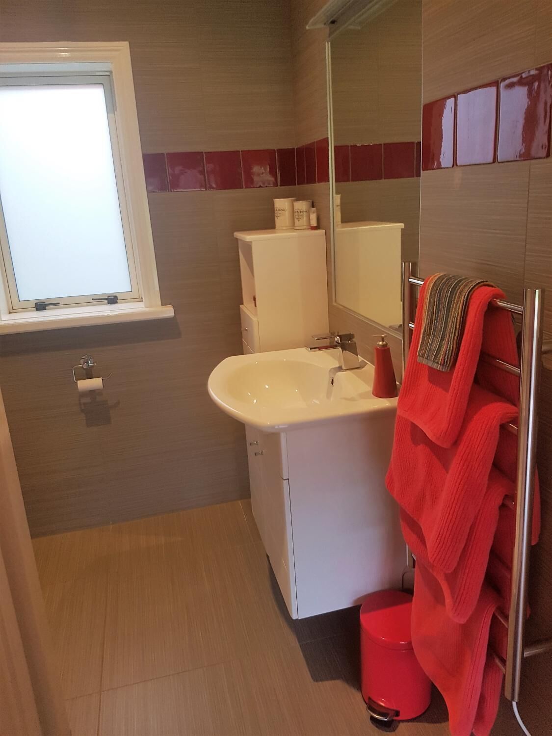 A bathroom with a white sink, a mirror, a red towel, and a red toilet.