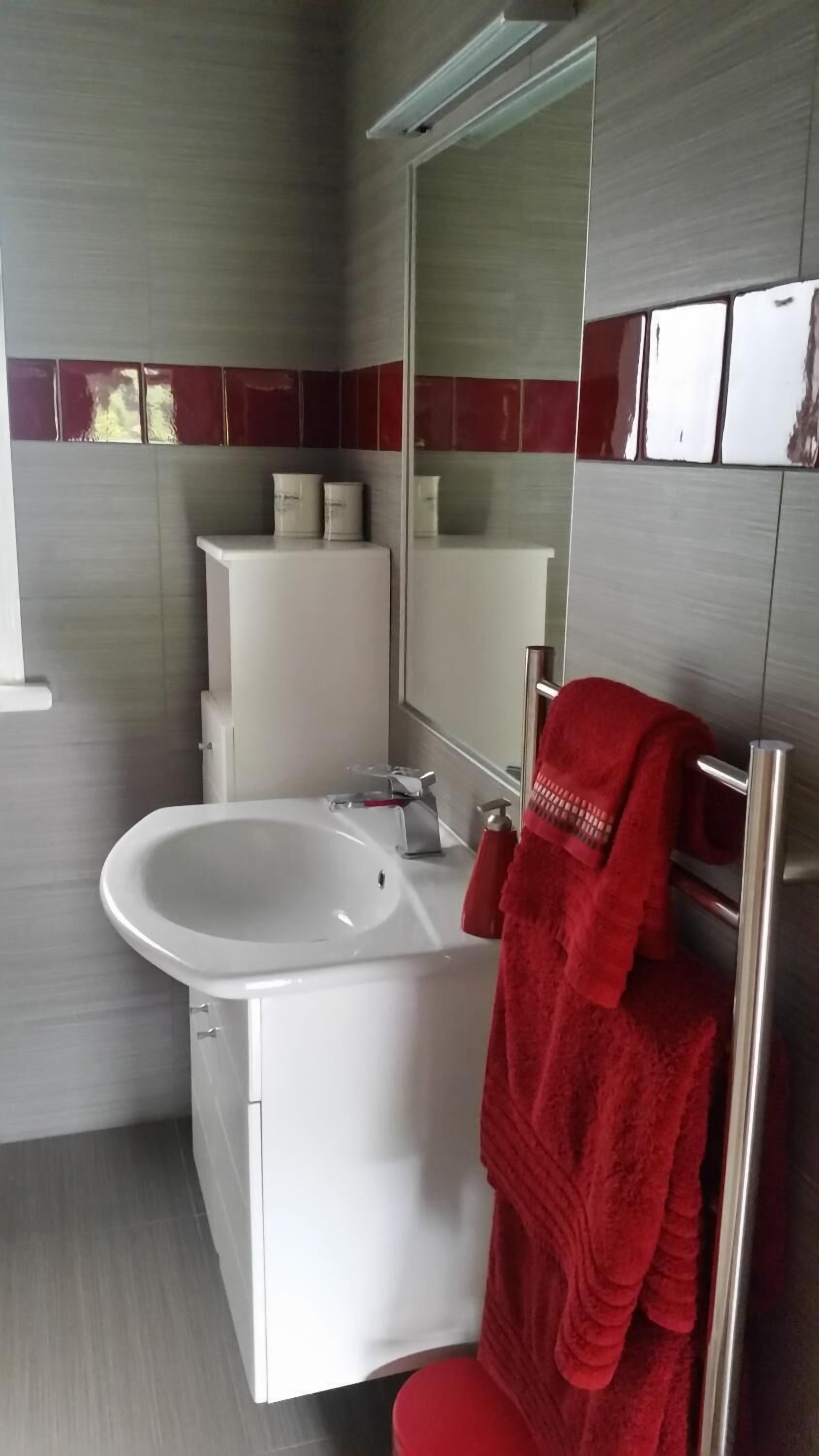 Een moderne badkamer met een wit wastafel, spiegel en rode handdoeken.
