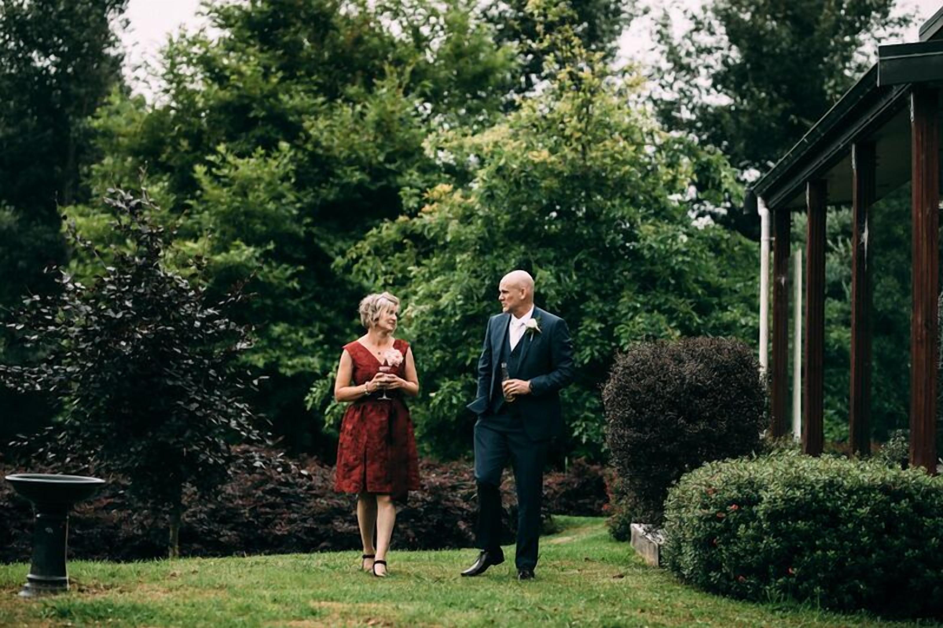 A couple standing in a garden with a gazebo in the background.