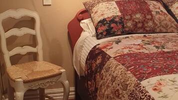 A bedroom with a bed, a chair, a window with blinds, and a wall-mounted light fixture.