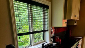 A kitchen with a large window, white cabinets, and a black countertop. - Matai Huka Boutique Accommodation (Paraparaumu)