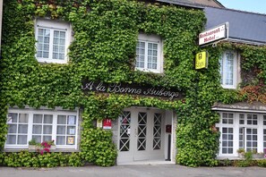 Un bâtiment aux murs couverts de lierre, sur lequel on peut lire l’inscription « À la Bonne Auberge ».