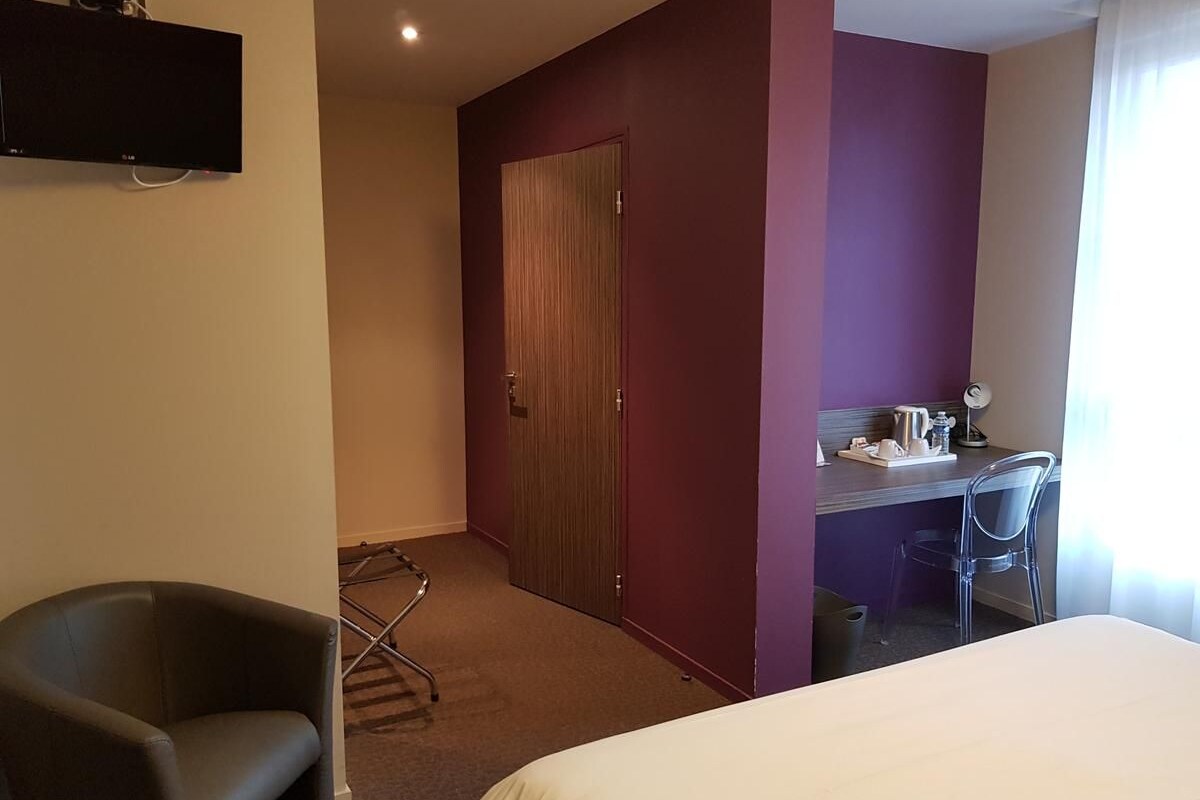 Hotellihuone, jossa on sänky, työpöytä tuolilla, televisio ja vaatekaappi.