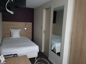 Une chambre d’hôtel avec un lit, une table de chevet, un miroir et une porte.