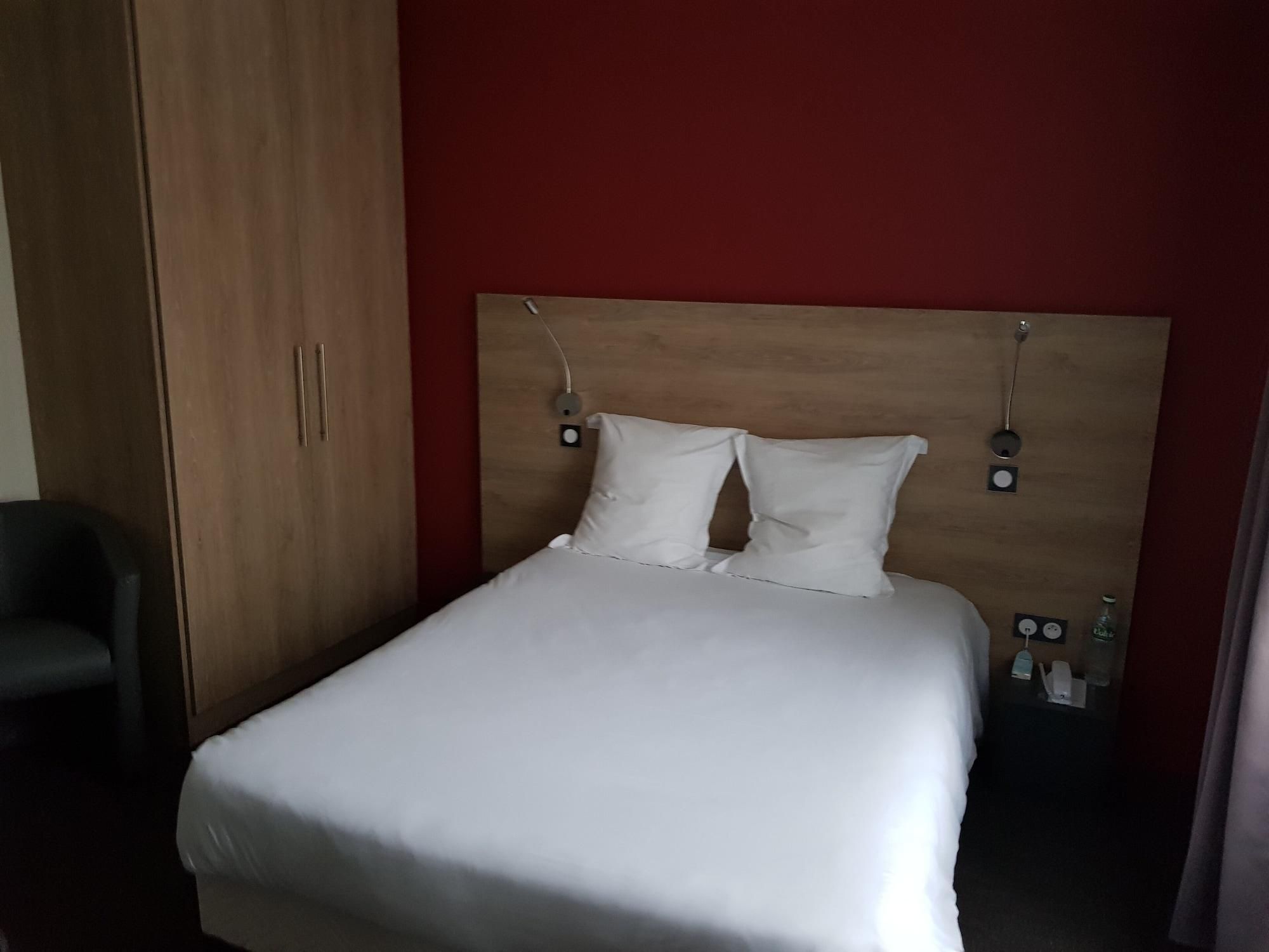 A single bed with white bedding, a wooden headboard, and a red wall.