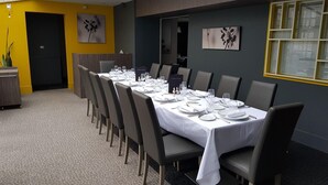 A dining area with a long table set for a meal, chairs, and a small plant on the left. - Logis La Bonne Auberge (Laval)