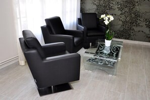 A modern waiting area with black leather chairs, a glass coffee table, and a potted orchid. - Logis La Bonne Auberge (Laval)