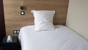 A neatly made bed with white bedding and pillows, a wooden headboard, and a bedside table with a remote control.