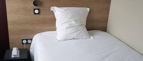 Ein ordentlich bezogenes Bett mit weißer Bettwäsche und Kissen, ein Holzkopfteil und ein Nachttisch mit Fernbedienung.