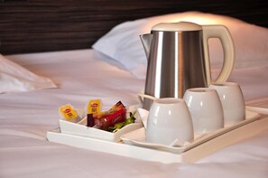 Un plateau avec une bouilloire électrique argentée, quatre tasses blanches et un assortiment de collations, notamment des sachets de thé Lipton et une petite salade.