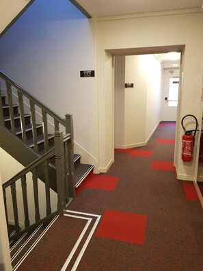 A hotel corridor with a staircase on the left, red carpeted floors, and fire extinguishers on the right. - Logis La Bonne Auberge (Laval)