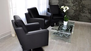 A modern waiting area with black leather chairs, a glass coffee table, and a potted orchid. - Logis La Bonne Auberge (Laval)