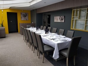 A dining area with a long table set for a meal, chairs, and a small plant on the left. - Logis La Bonne Auberge (Laval)