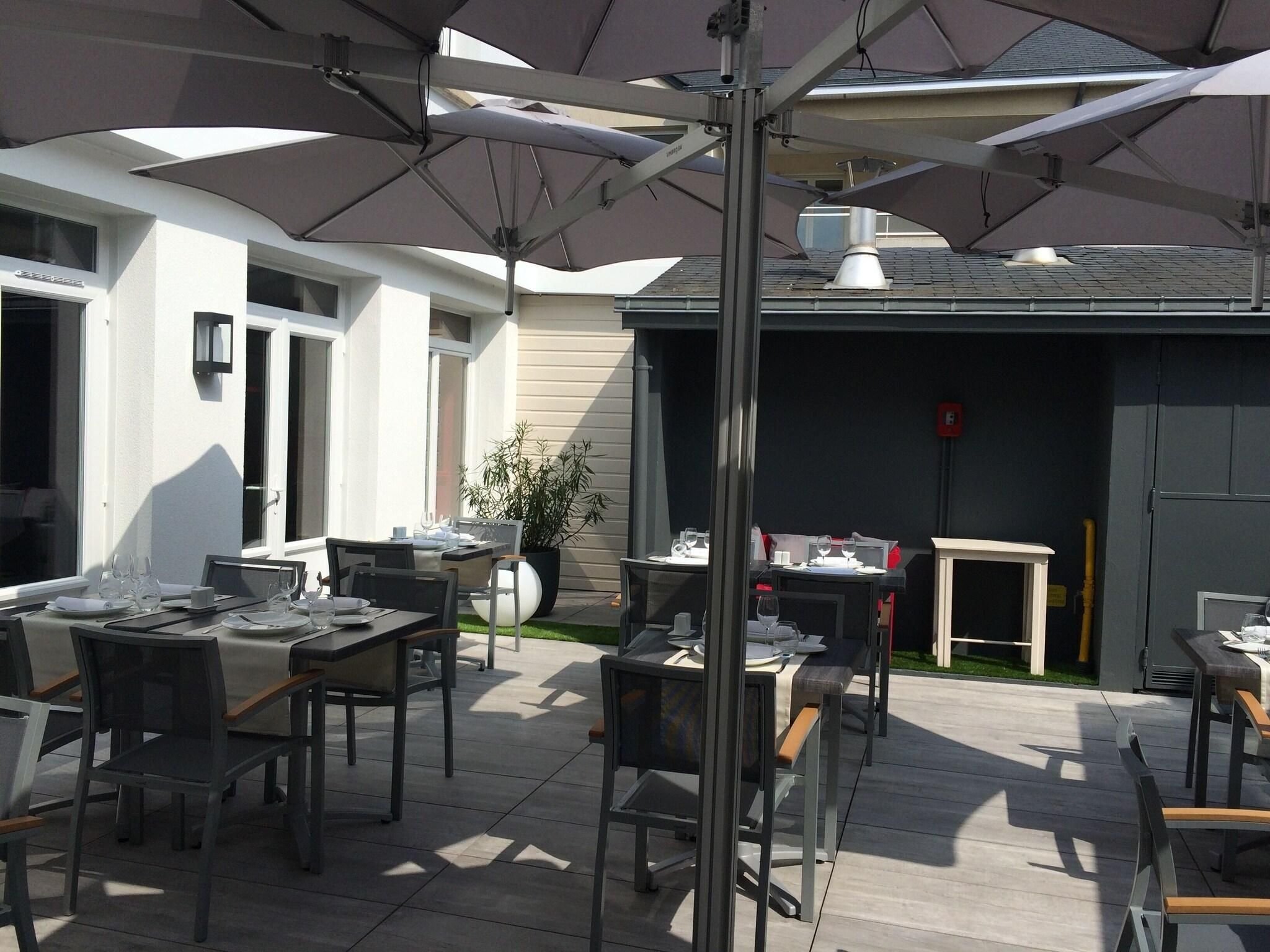 An outdoor patio area with tables and chairs, umbrellas, and a potted plant.