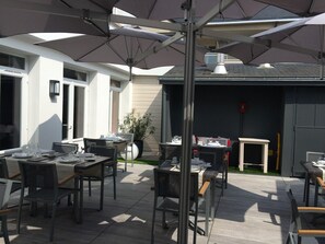 Un espace extérieur aménagé en terrasse, avec des tables et des chaises, des parasols et un pot de fleurs.