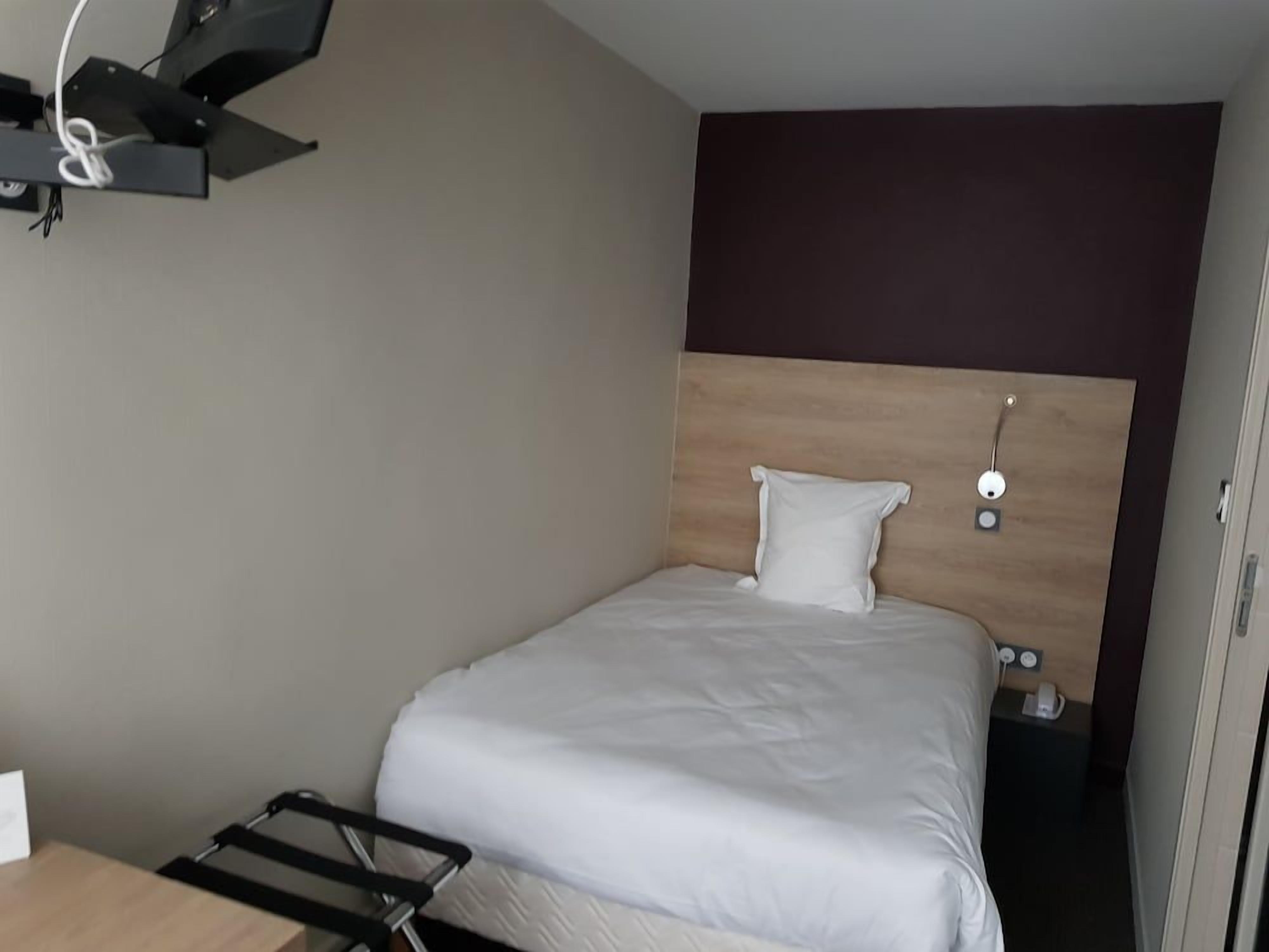 Une chambre d’hôtel équipée d’un lit, d’une table de chevet, d’une lampe fixée au mur et d’une prise électrique.