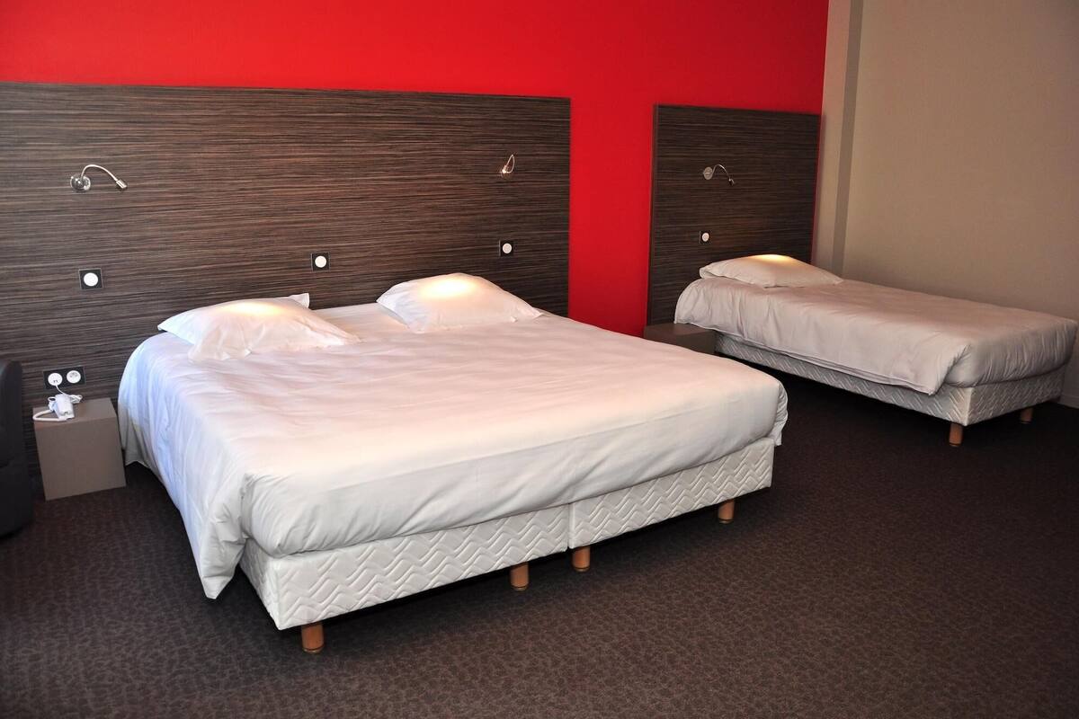 A hotel room with two beds, a red accent wall, and a dark wooden headboard.