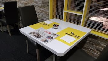 A table with a newspaper, cutlery, and a bowl.
