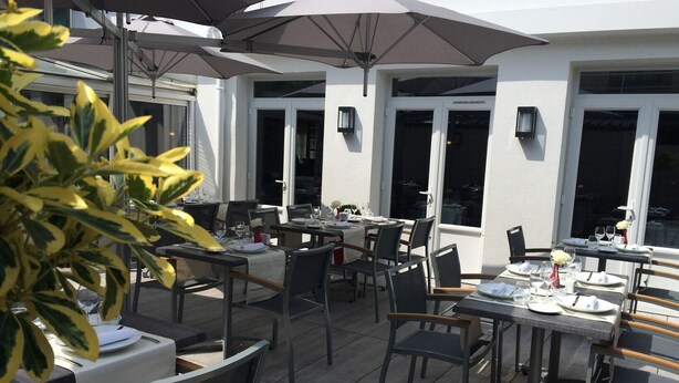 An outdoor dining area with tables and chairs, umbrellas, and potted plants. - Logis La Bonne Auberge (Laval)