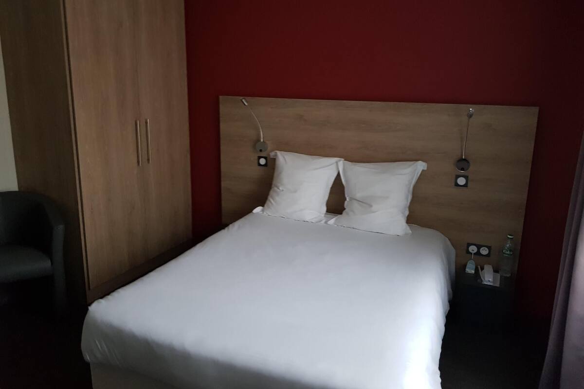 A neatly made bed with white linens, a wooden headboard, and two bedside lamps.