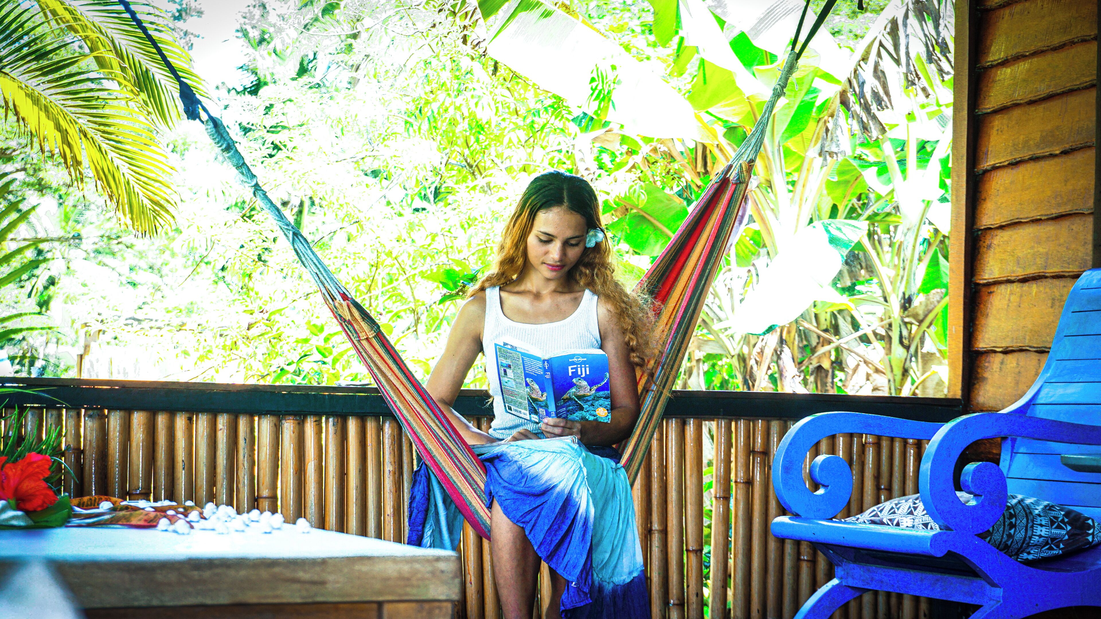 A person sitting in a hammock reading a book, with a wooden fence and greenery in the background.