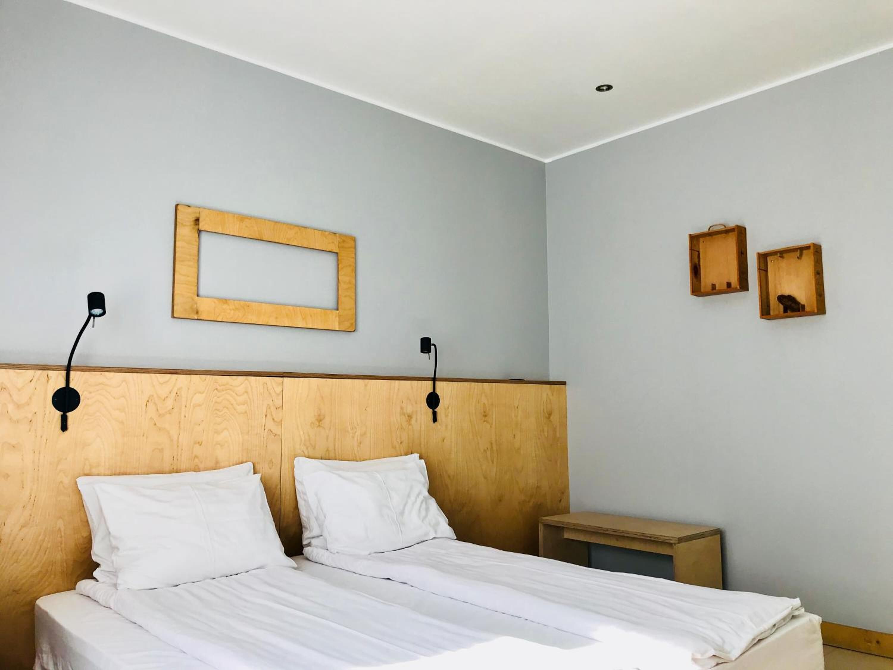 A bedroom with a wooden headboard, two bedside tables, a bed with white linens, and two wall-mounted light fixtures.