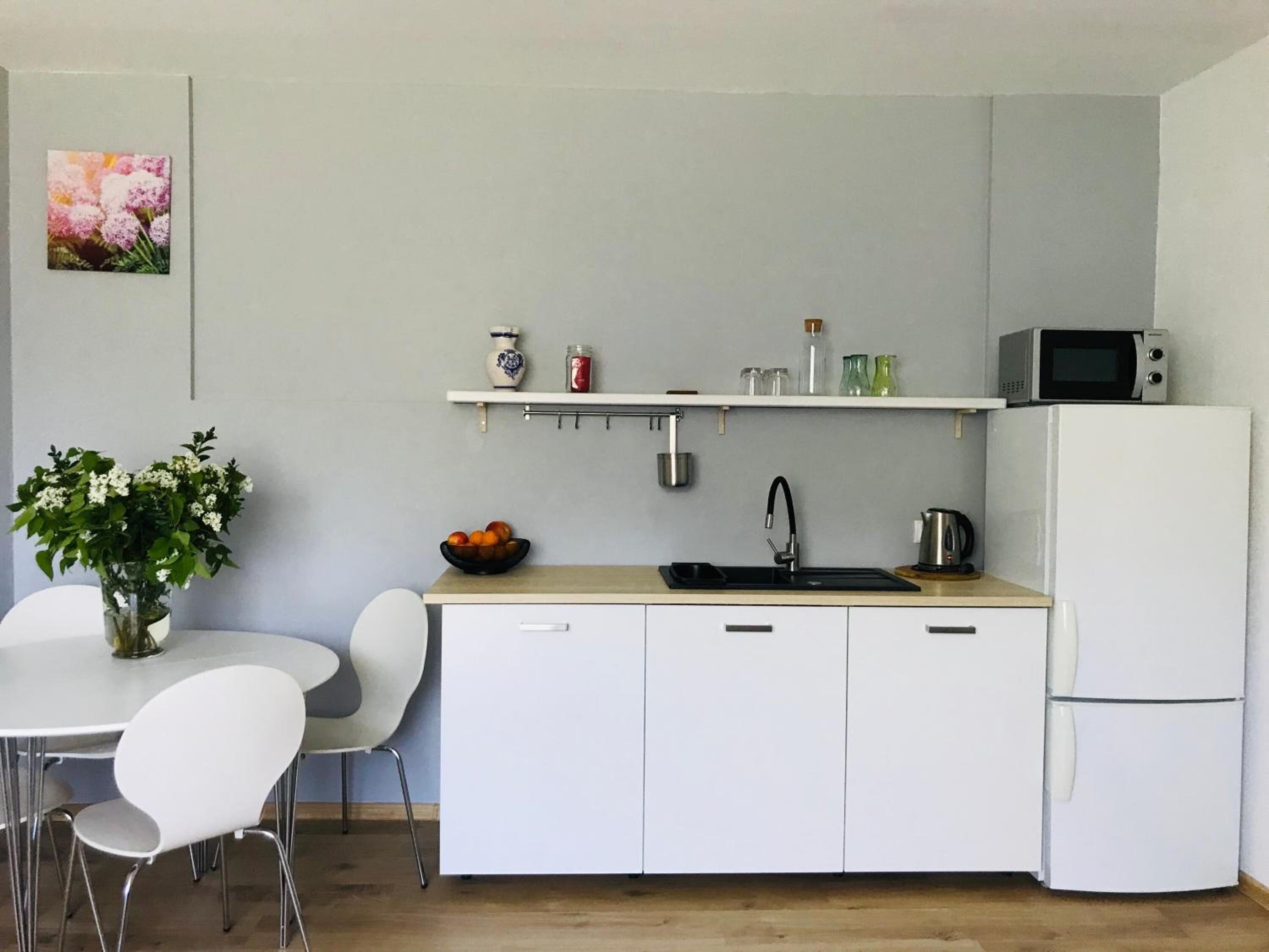 Cocina compacta con armarios blancos, un lavabo, un microondas y un refrigerador. Hay una pequeña repisa sobre el lavabo con diversos objetos.