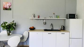 Cocina compacta con armarios blancos, un lavabo, un microondas y un refrigerador. Hay una pequeña repisa sobre el lavabo con diversos objetos.