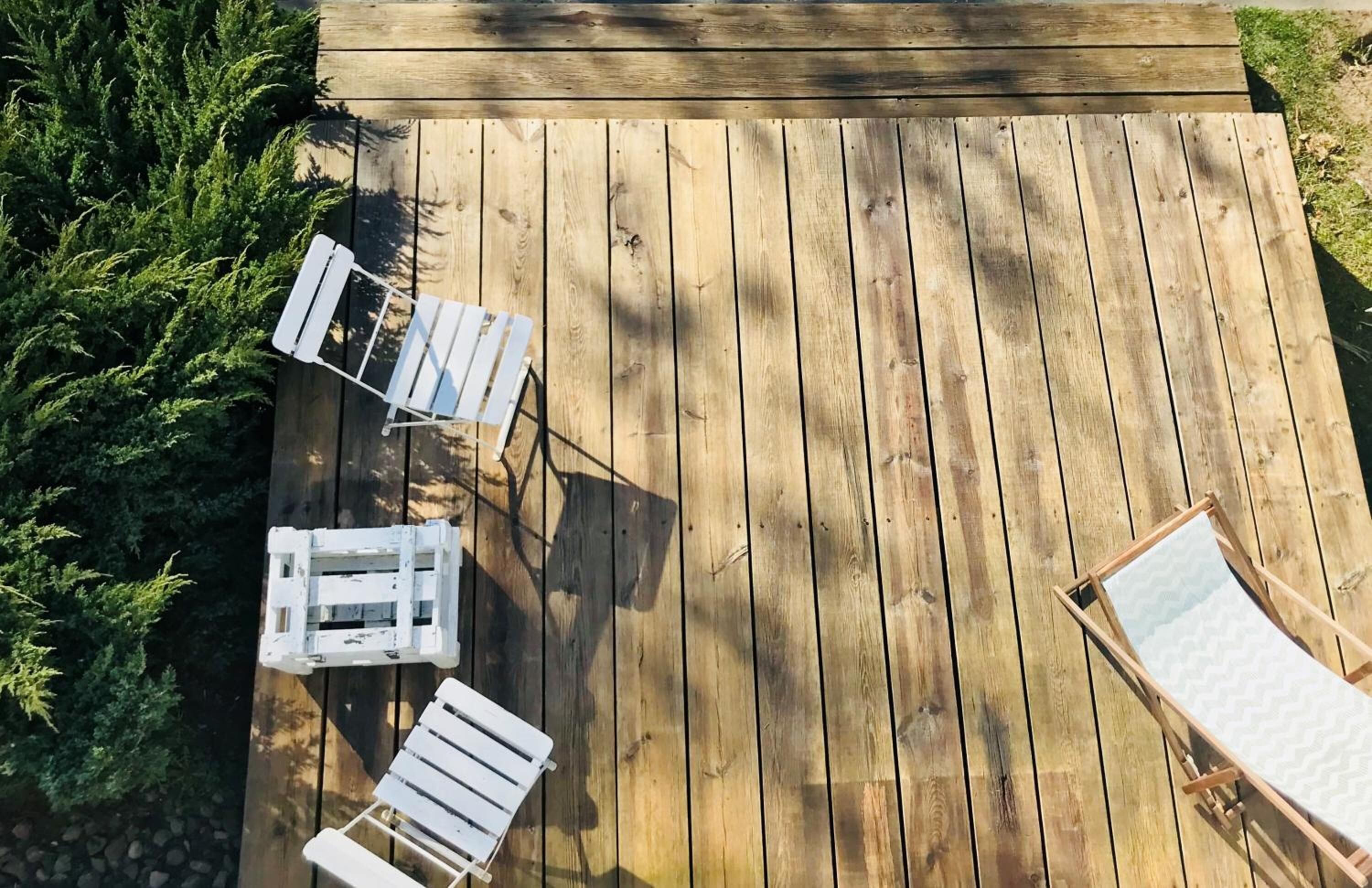 Una terraza de madera con tres sillones blancos y una mesita.