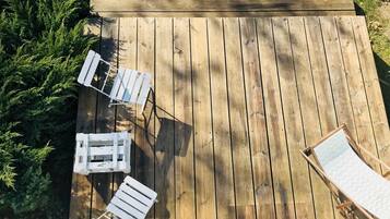 Una terraza de madera con tres sillones blancos y una mesita.