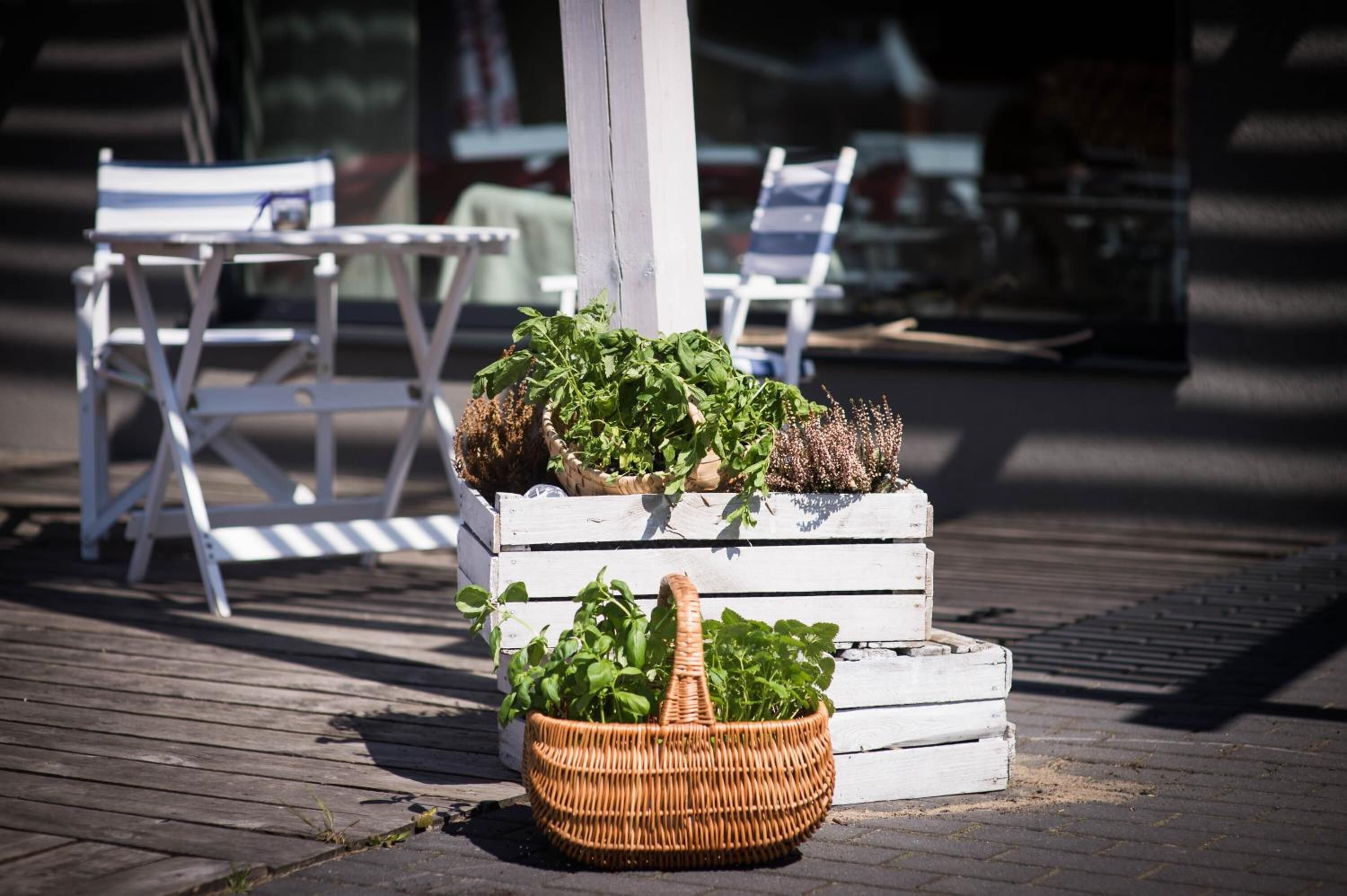 Une terrasse en bois avec des meubles d’extérieur et un panier en osier rempli de plantes.