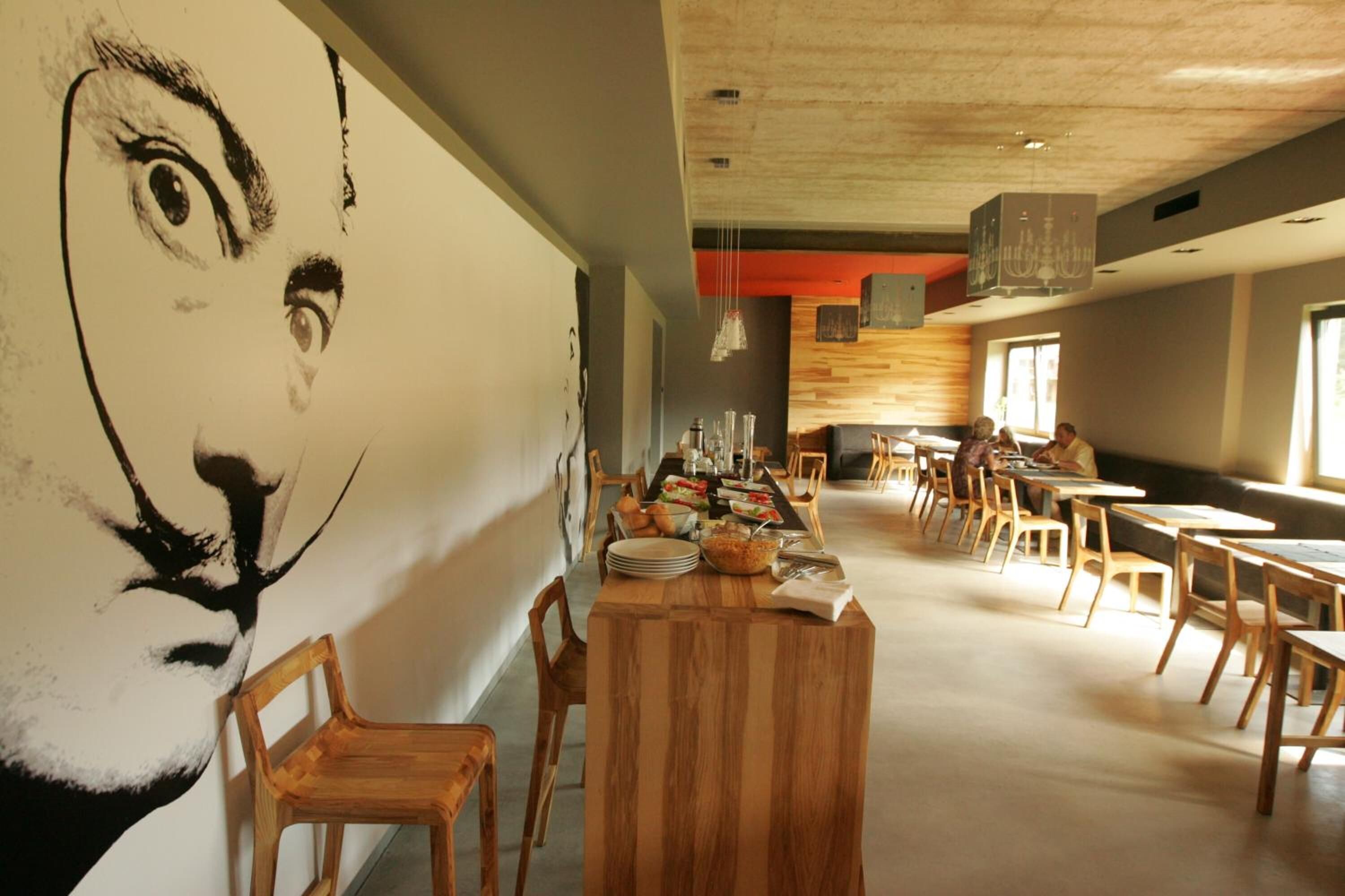 Comedor con mesas y sillas de madera, un mural grande en la pared y un diseño de techo moderno.
