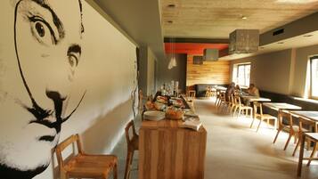 Comedor con mesas y sillas de madera, un mural grande en la pared y un diseño de techo moderno.