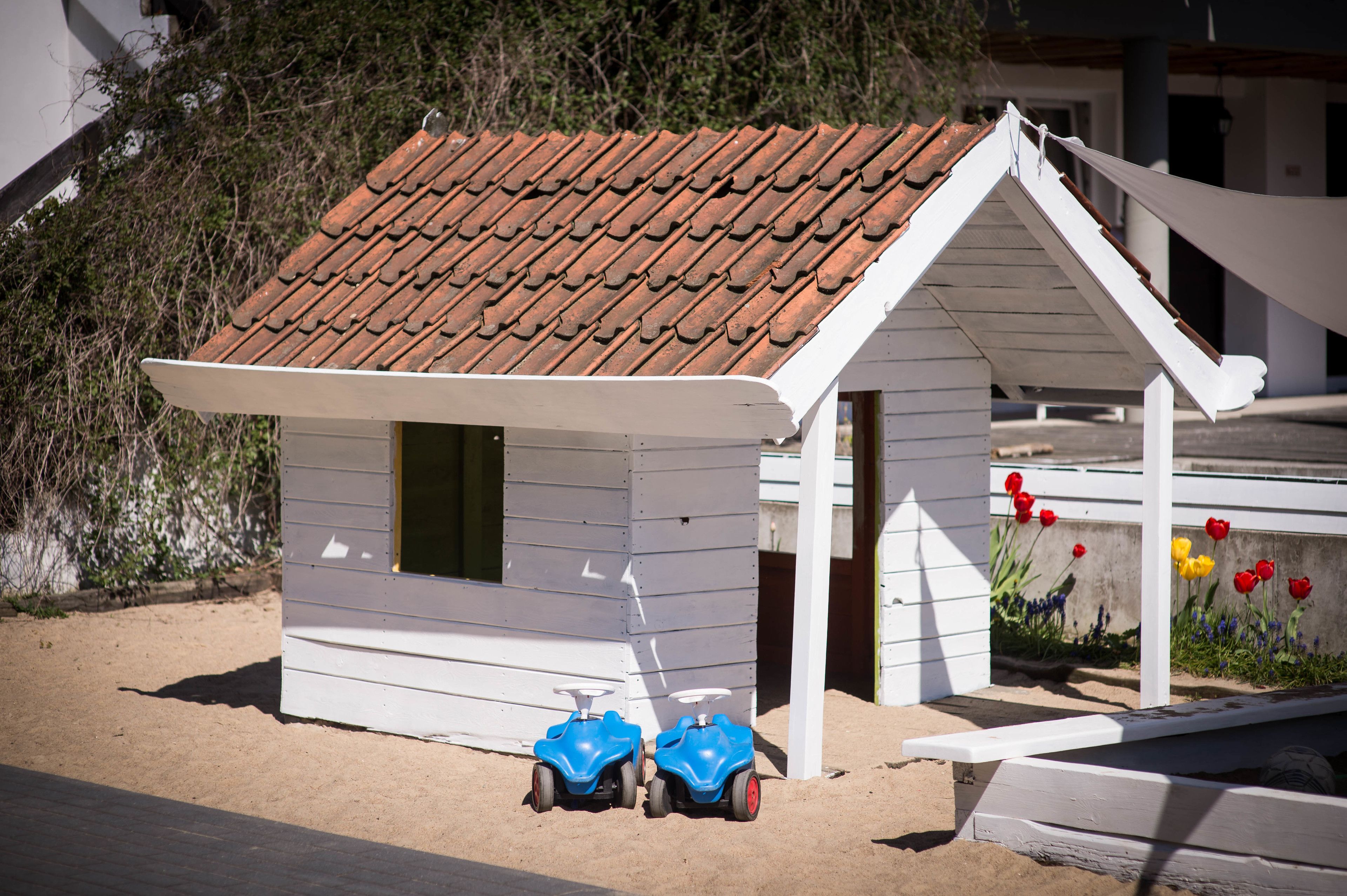 A small beach hut with a tiled roof and a white exterior. Two blue scooters are parked in front.