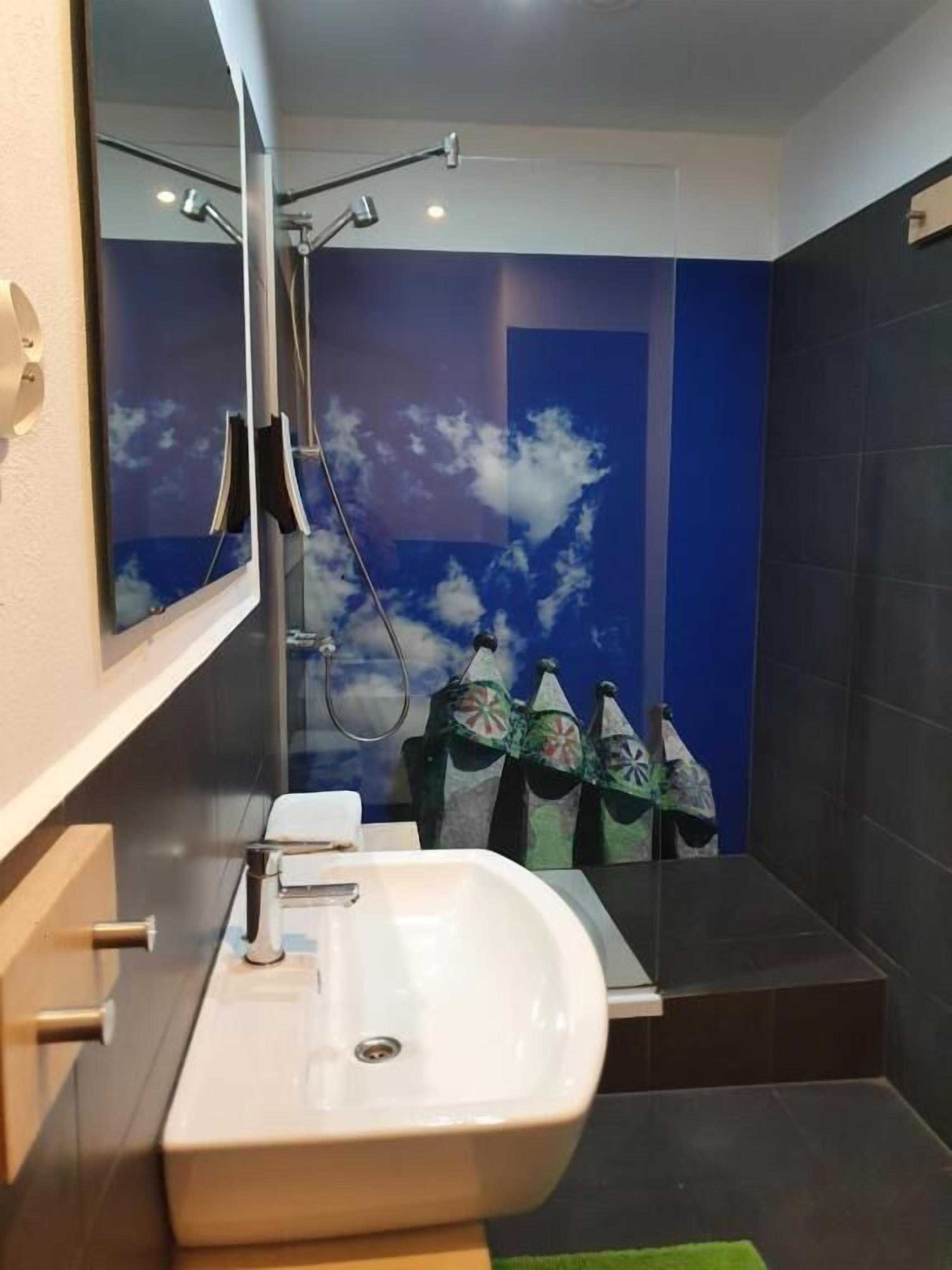 Une salle de bain moderne avec un grand miroir, un lavabo blanc et une douche dotée d’une porte en verre.