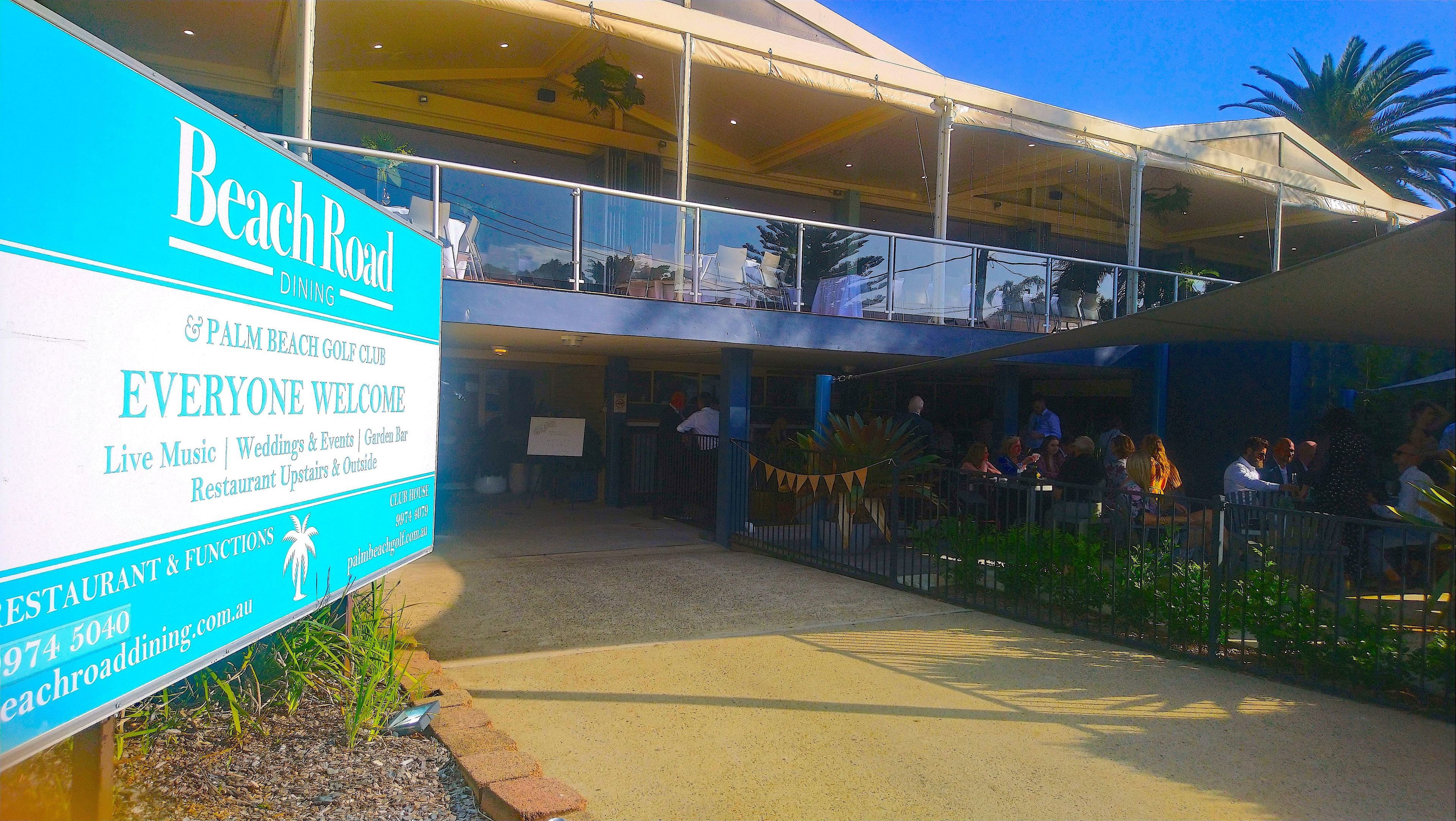 Un edificio de dos pisos con un letrero que anuncia 'Beach Road Dining' y 'Palm Beach Golf Club'.